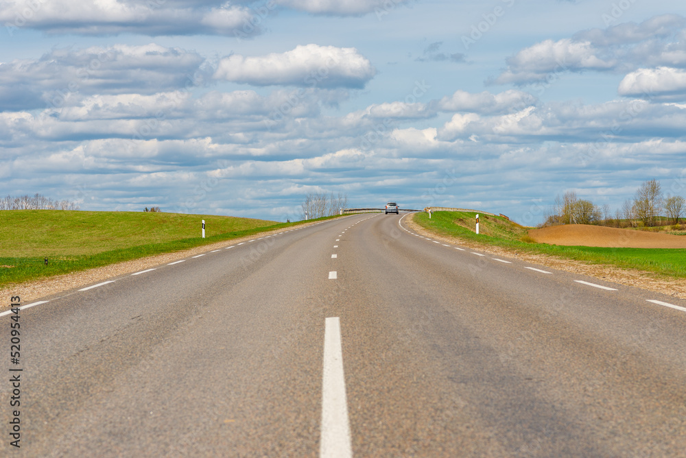 Cars asphalt road through the green agricultural fields background on a sunny summer day.