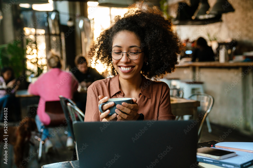 Young african american woman using laptop and drinking coffee in cafe Young african american woman using laptop and drinking coffee in cafe