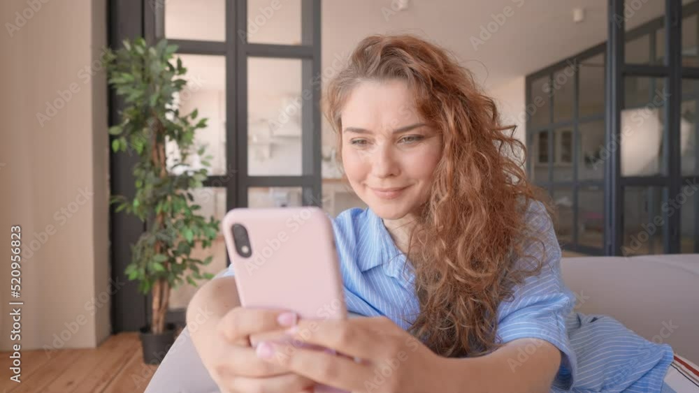 lady with red curly hair using smartphone at home messaging online happy smiling sitting on sofa in living room at home technology for communication lady with red curly hair using smartphone at home messaging online happy smiling sitting on sofa in living room at home technology for communication
