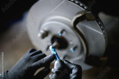 Auto mechanic applying silicone brake lubricant on the brake caliper slide pins.