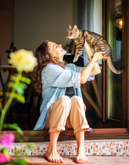 Young beautiful woman holding a gray cat in her hands sitting on terrace of country house
