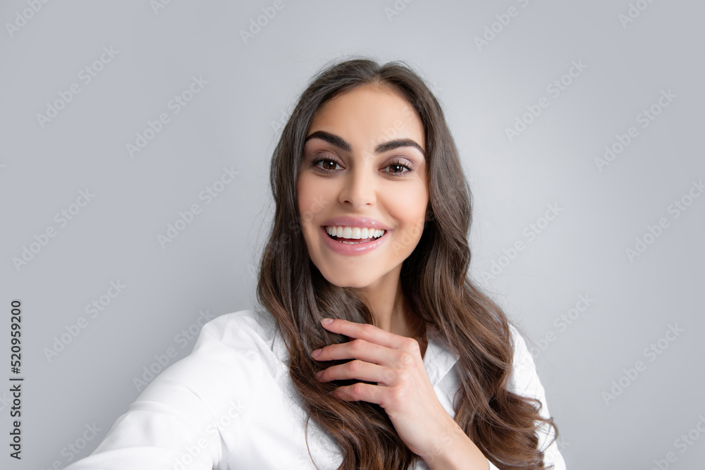 Pleasant girl making selfie in studio and laughing. Good-looking young woman with brown wavy hair taking picture of herself on gray background. Pleasant girl making selfie in studio and laughing. Good-looking young woman with brown wavy hair taking picture of herself on gray background.