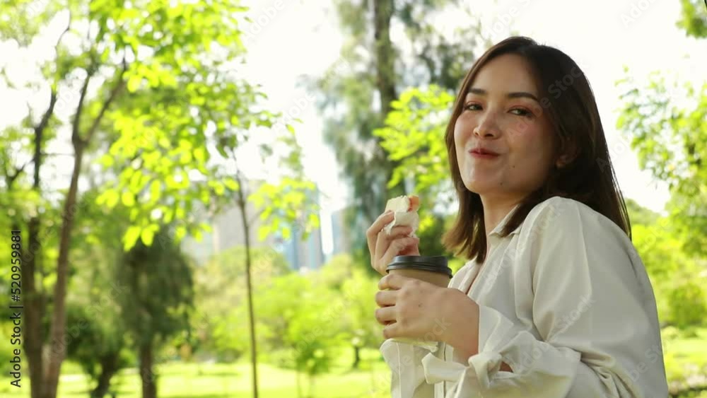 Beautiful Asian woman eats sandwiches and hot coffee in the garden with deliciousness and smiles for the camera. Beautiful Asian woman eats sandwiches and hot coffee in the garden with deliciousness and smiles for the camera.