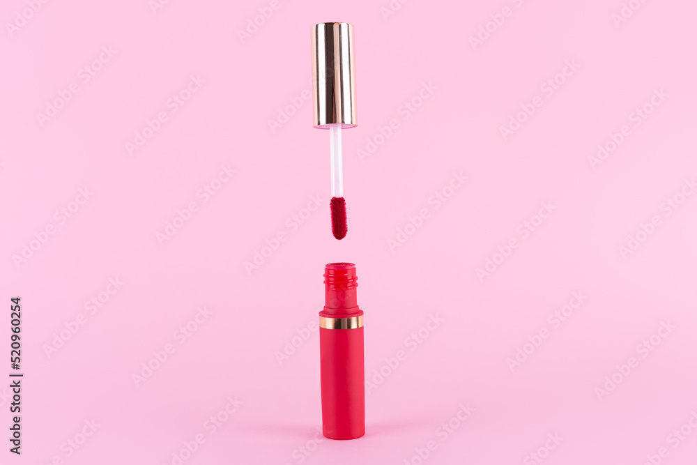 Lipstick and applicator wand on pastel pink background. Liquid lip stick red lip gloss open tube. Makeup cosmetic product. Top view, flat lay, copy space - obrazy, fototapety, plakaty 