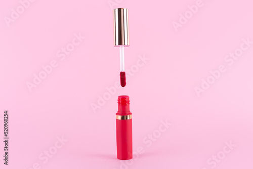 Lipstick and applicator wand on pastel pink background. Liquid lip stick red lip gloss open tube. Makeup cosmetic product. Top view, flat lay, copy space photo