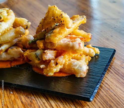 Detalle de verduras en tempura listas para comer en restaurante sobre pizarra negra en meda de madera photo