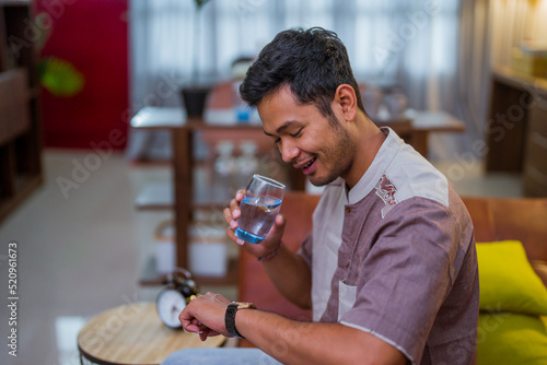 happy muslim male waiting to break his fasting holding a glass of water while looking at his watch