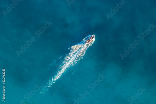 Top view from drone of fast sailing yacht, speed boat cruising in high speed in clear blue water in summer. Aerial view. Summer vacation at sea, travel background