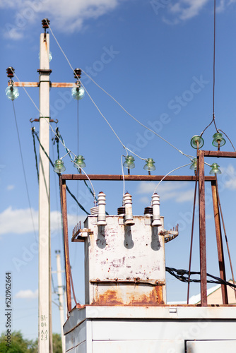 A metal rusty white elecrical transformer with wires going towards it agaisnt a blue clear sky and an electrical pole photo