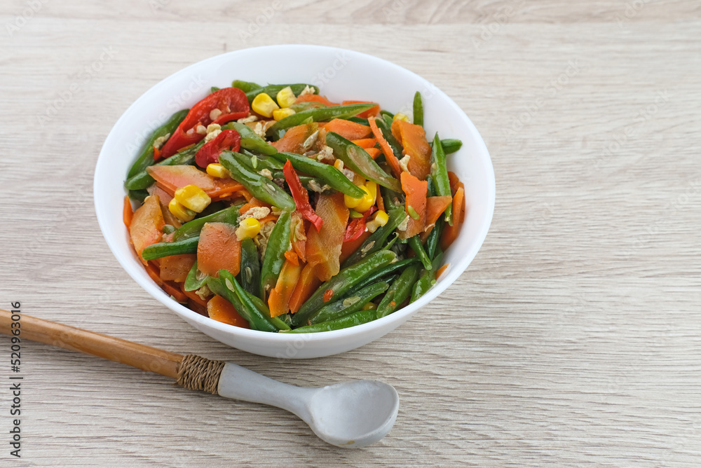 Orak arik sayur or stir fried vegetables with carrot, bean, corn and egg. Served in white bowl on wooden background. Orak arik sayur or stir fried vegetables with carrot, bean, corn and egg. Served in white bowl on wooden background.