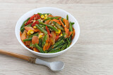 Orak arik sayur or stir fried vegetables with carrot, bean, corn and egg. Served in white bowl on wooden background. 