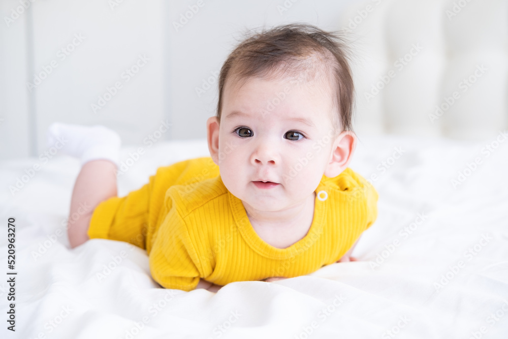healthy asian baby girl 5 months in yellow bodysuit on bed on white bedding healthy asian baby girl 5 months in yellow bodysuit on bed on white bedding