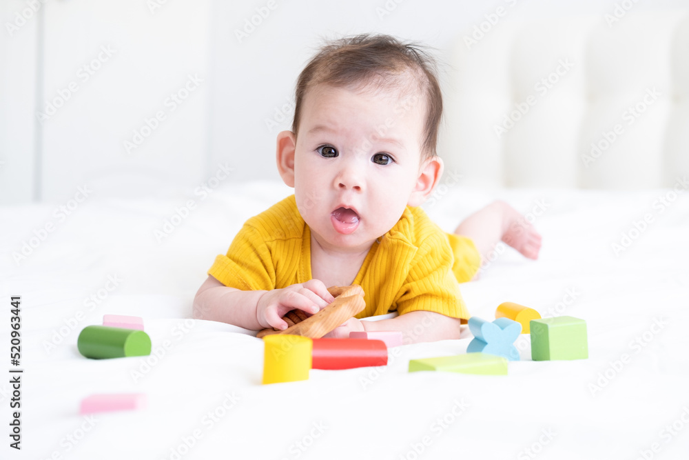 healthy asian baby girl in yellow bodysuit playing with wooden toys on white bedding healthy asian baby girl in yellow bodysuit playing with wooden toys on white bedding
