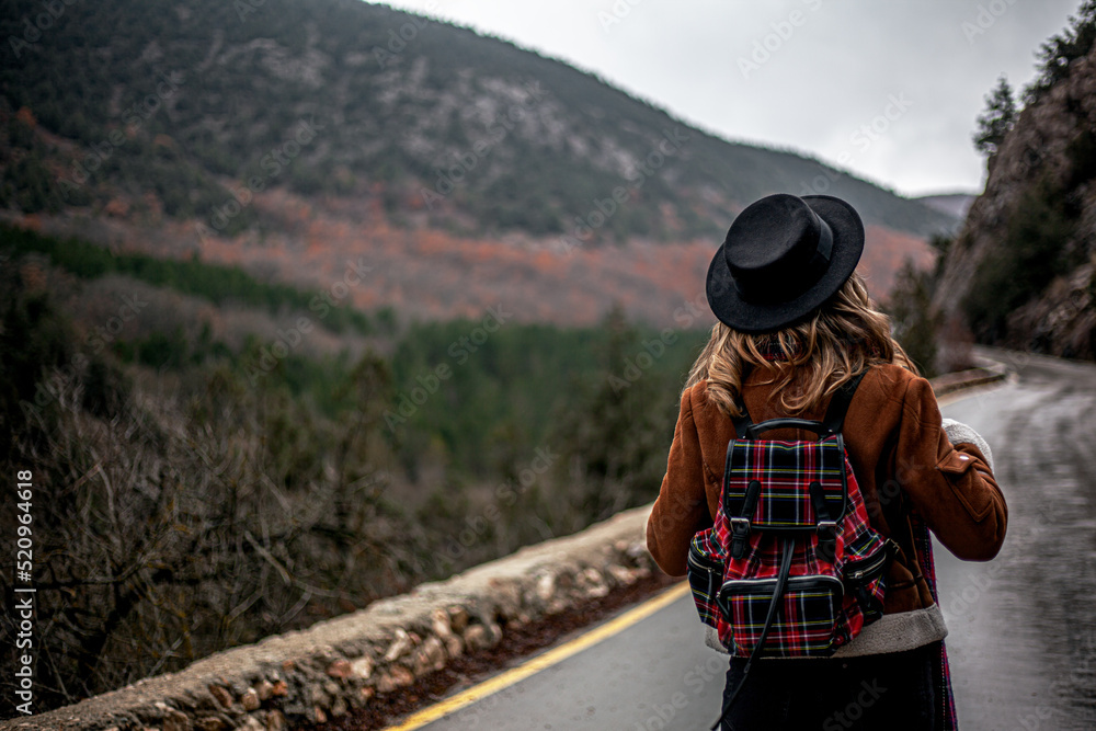 Woman walking in the road against the fall forest, girl dressed style clothes, hat and scarf