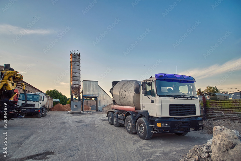 Concrete batching and manufacture plant, parked mixer trucks at the plant yard, ready to deliver concrete products. Ready-mix concrete plant. Construction industry concept.