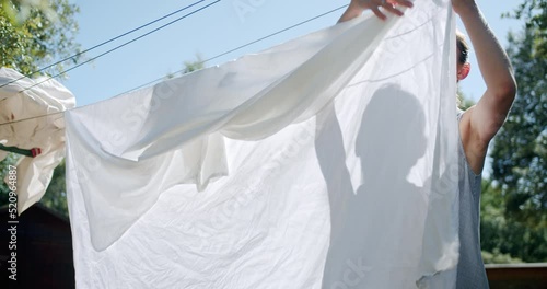 Young Pretty Woman Hanging Up Clean Bed Sheets Clothes On Clothesline in Countryside in summer day.High quality 4k footage