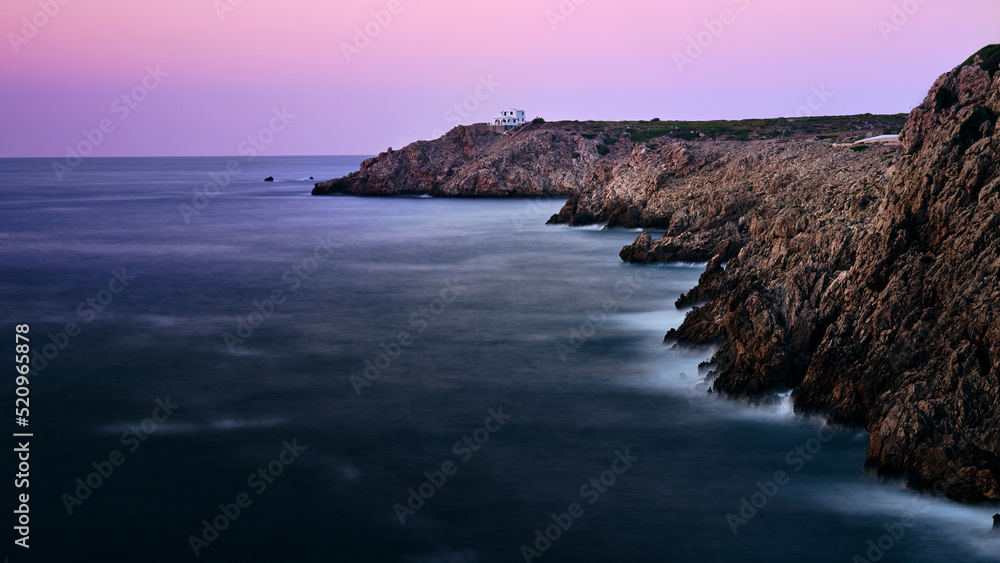 The rocky coast of Menorca island and the house at the end of the cliff, Spain