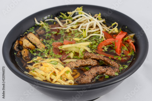 Korean dish soup with noodles, meat and soybean sprouts in a black plate
