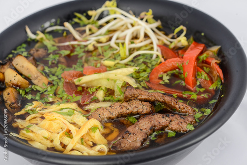 Korean dish soup with noodles, meat and soybean sprouts in a black plate, macro photo
