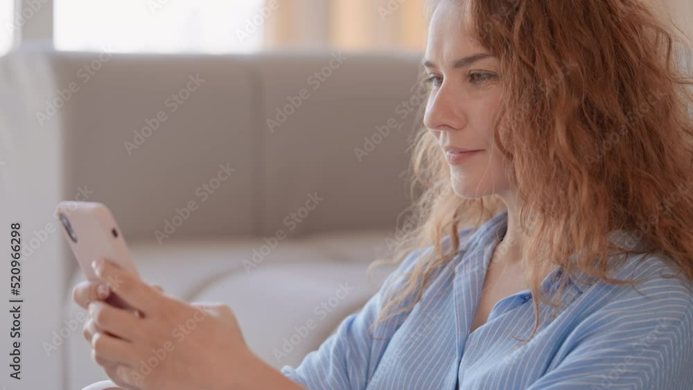 closeup woman with curly red hair using smartphone scrolling news feed social media or chat with friend online at home closeup woman with curly red hair using smartphone scrolling news feed social media or chat with friend online at home