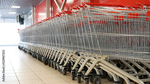 Close-up of many steel shopping trolleys with red handles standing in a row
