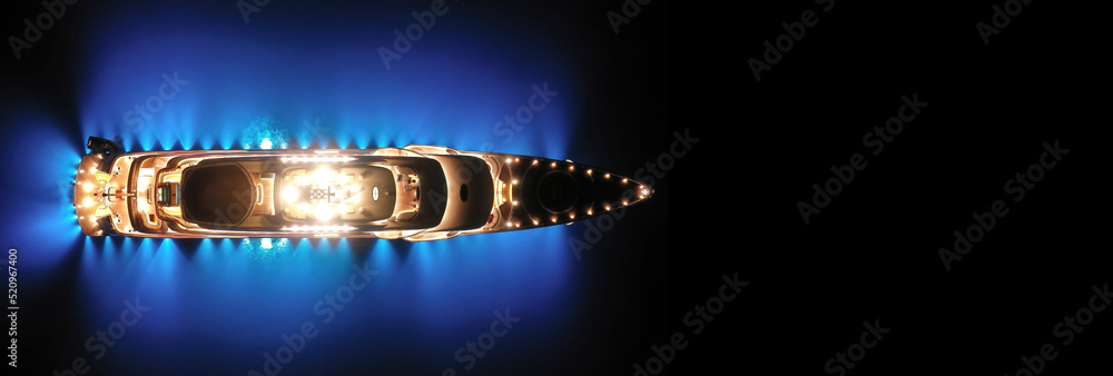 Aerial drone ultra wide panoramic night shot with copy space of beautiful latest technology modern led illuminated luxury mega yacht anchored in tropical exotic bay with deep blue sea