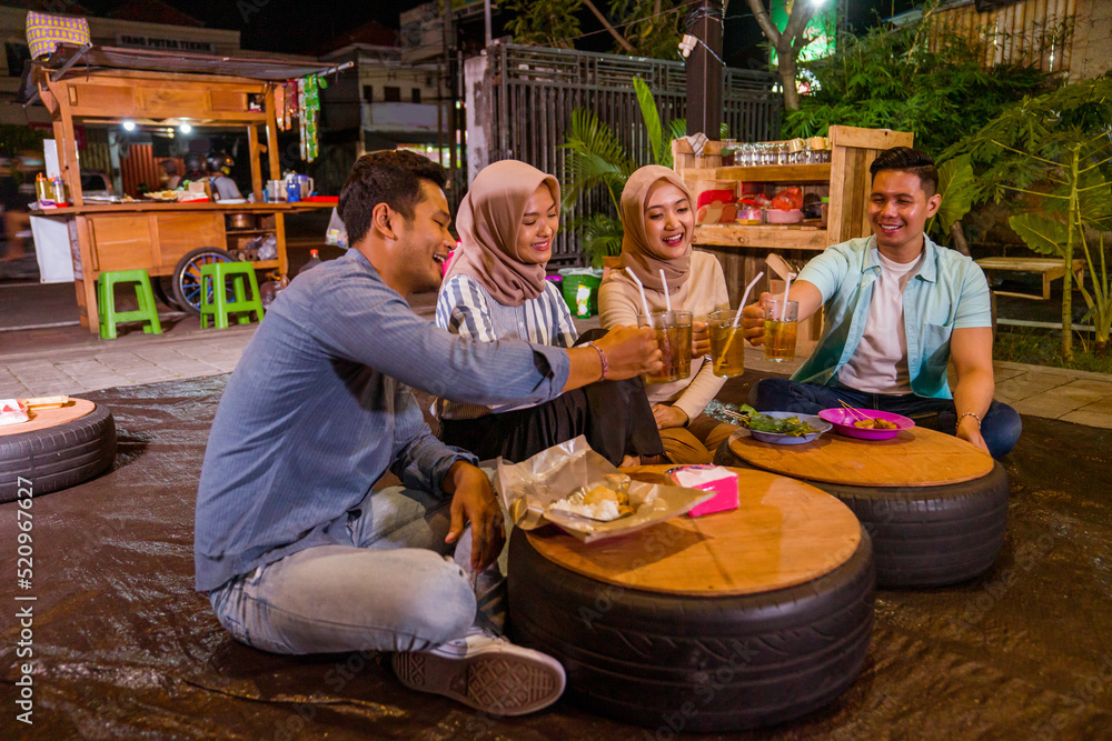 portrait of happy muslim friend enjoy having iftar dinner at traditional food stall sitting on the floor and cheering the drink portrait of happy muslim friend enjoy having iftar dinner at traditional food stall sitting on the floor and cheering the drink