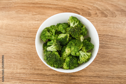 Fresh raw broccoli ready to cook served on white plate on wooden background. 