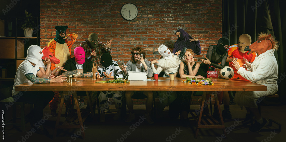 Group of people standing, sitting at the long table in different costumes, indoors and lively communicating.