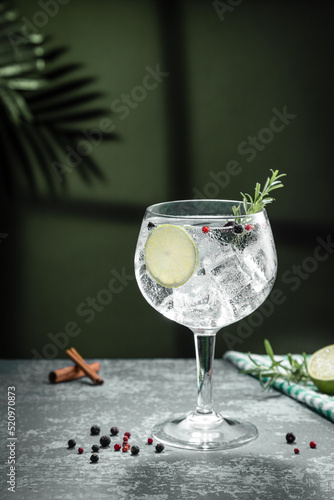 Gin tonic cocktail and shadows next to the window on dark concrete background. Vertical format.