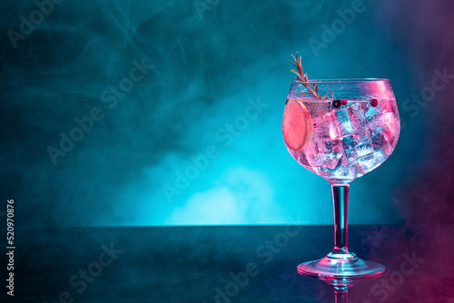 Cold gin tonic under pink and blue light illumination on smoky background with copy space. photo