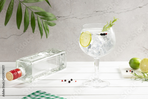 Cold glass of gin tonic and bottle on white wooden base on light background. photo