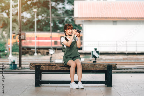Portrait Young asian woman smiling tourist Traveler girl walking and with a holding the camera waits train travel journey is taken in railway platform Thailand, summer relax vacation Concept. © Thinapob