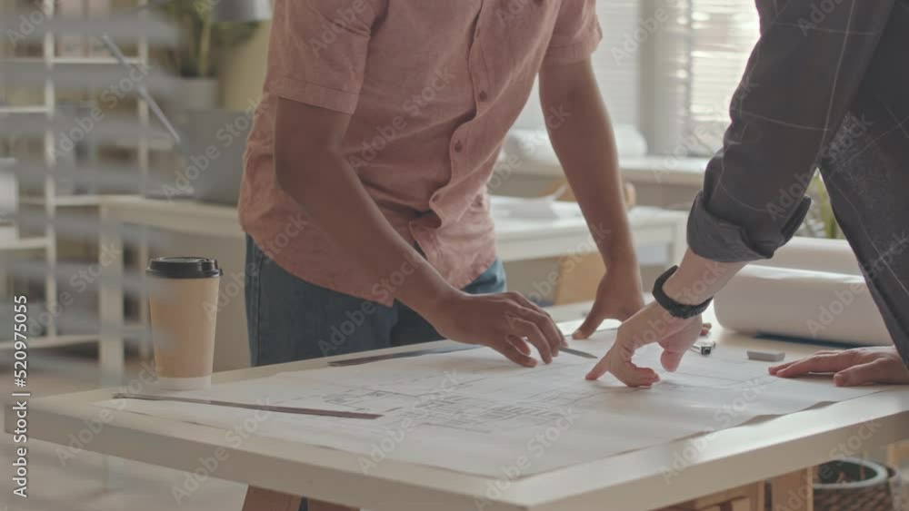 Midsection slowmo of two unrecognizable architects developing drawing plan of building on rolled out sheet of paper on office desk Midsection slowmo of two unrecognizable architects developing drawing plan of building on rolled out sheet of paper on office desk