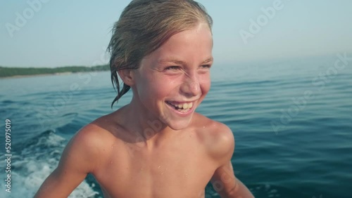 Close up portrait of happy kid riding a boat in the sea during summer vacation, authentic laughter and emotion.