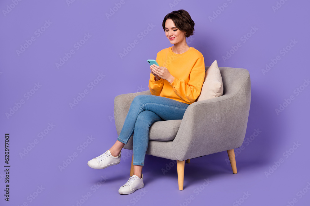 Portrait of attractive cheerful trendy girl sitting in chair using gadget 5g post isolated over violet lilac color background Portrait of attractive cheerful trendy girl sitting in chair using gadget 5g post isolated over violet lilac color background