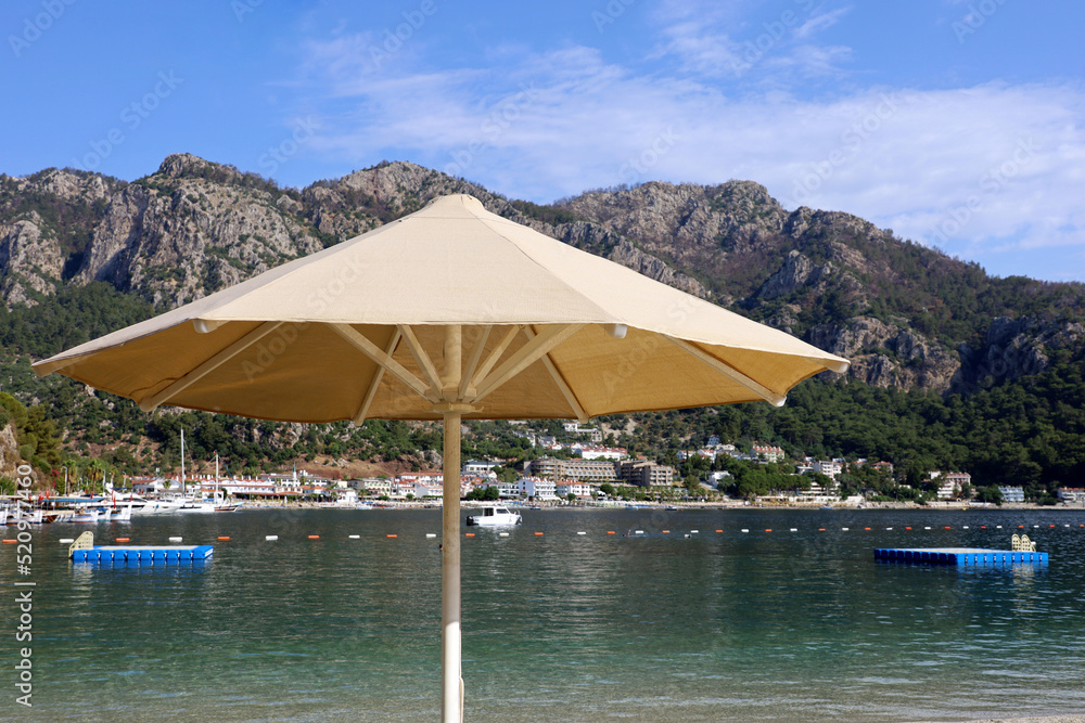 Sun umbrella on sea beach. View to mountains on Mediterranean coast of Turkey, floating pontoons and resort town Sun umbrella on sea beach. View to mountains on Mediterranean coast of Turkey, floating pontoons and resort town