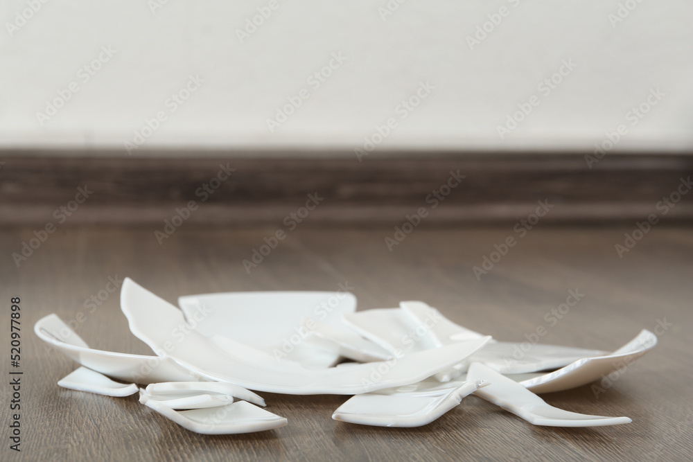 Pieces of broken ceramic plate on wooden floor indoors, space for text