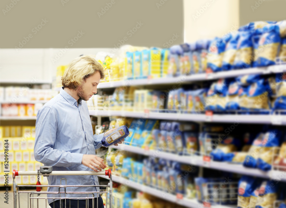 Young man shopping in supermarket, reading product information