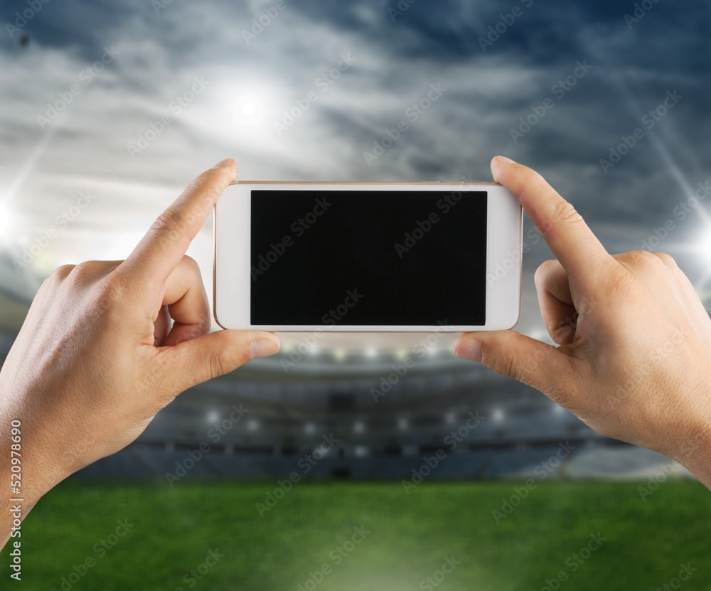Hand hold smartphone with a blank screen on the stadium background