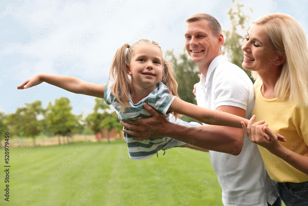 Cute little girl having fun with her parents in park on summer day