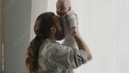 Caucasian bearded adult father throw up little cute smiling son daughter infant playing together at home tickling tummy of baby with nose dad holding newborn having fun with kid child tickle game photo