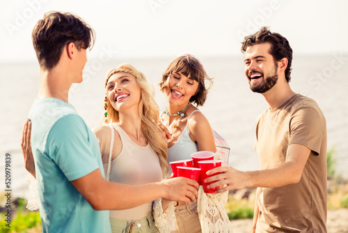 Portrait of cheerful carefree buddies embrace talk speak hold plastic alcohol cups enjoy free time outdoors