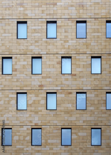 the facade of a modern stone building with geometric repeating pattern of small windows