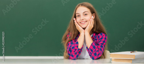 happy child sit at school on blackboard background, knowledge day. Banner of schoolgirl student. School child pupil portrait with copy space.