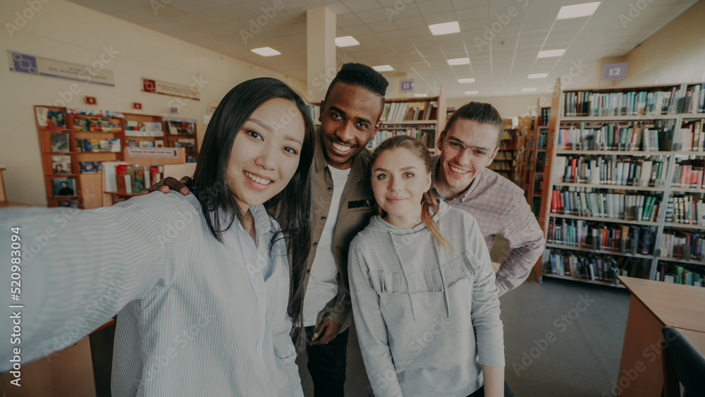 Obraz premium Point of view of international student group have fun smiling and taking selfie photos on smartphone camera at university library indoors