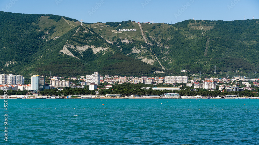 Panorama of city on shore of Gelendzhik Bay. Inscription 'Gelendzhik' on ridge of Caucasus Mountains. Forest grows on mountains.