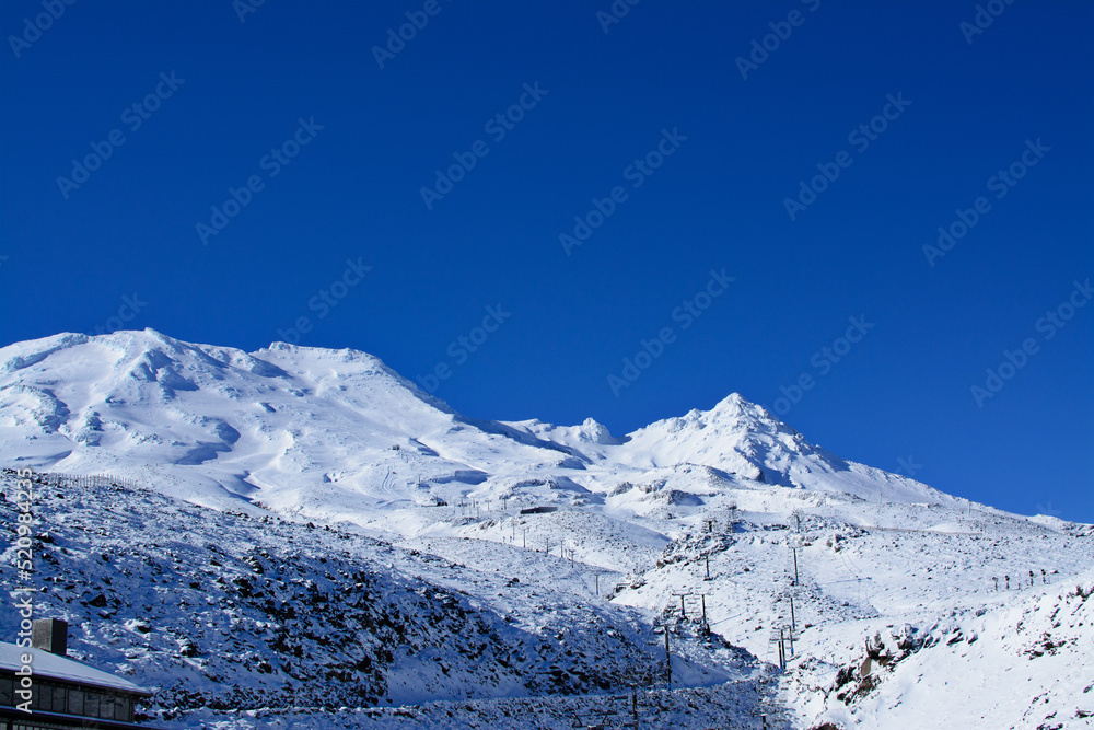 Ski resort at Mountain Ruapehu beautifully covered with snow. Majestic white-capped peaks against cloudless blue sky. Turoa, North Island of New Zealand on a bright winter day