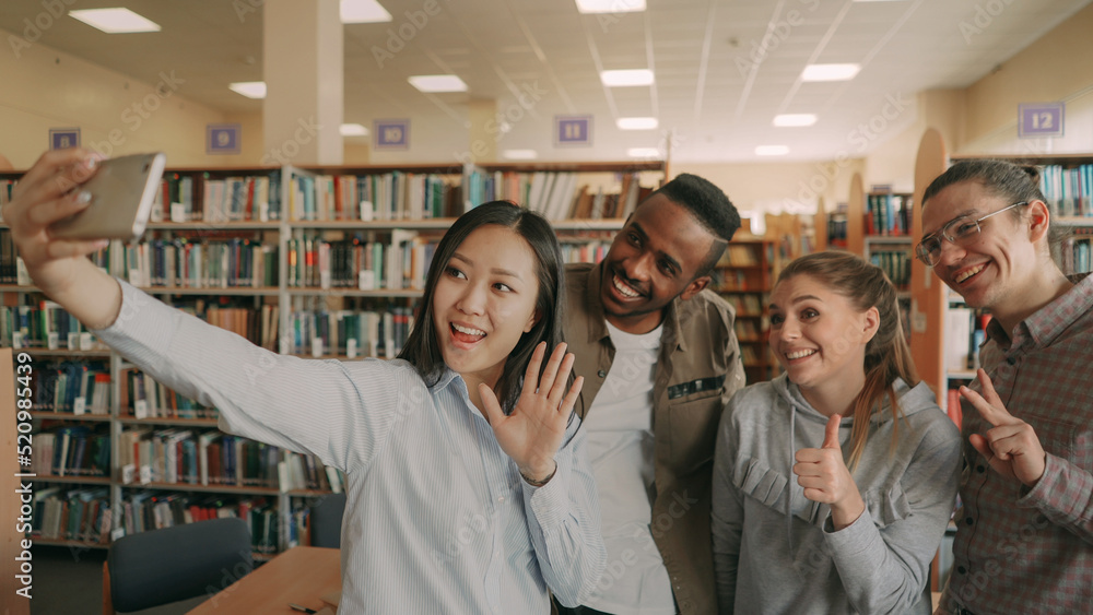 Group of international students have fun smiling and making selfie photos on smartphone camera at university library indoors. Cheerful friends have rest while preapre project together Group of international students have fun smiling and making selfie photos on smartphone camera at university library indoors. Cheerful friends have rest while preapre project together