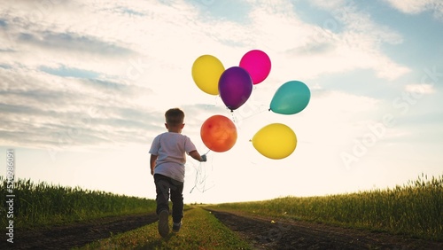 little baby boy run with balloons in the park in nature. happy family holiday birthday kid dream concept sun. a little baby with colorful balloons lifestyle run with the road in the field park